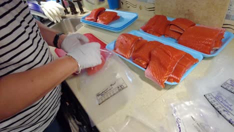 gloved hands putting fresh sockeye salmon fillets into plastic bags to be vacuum sealed later