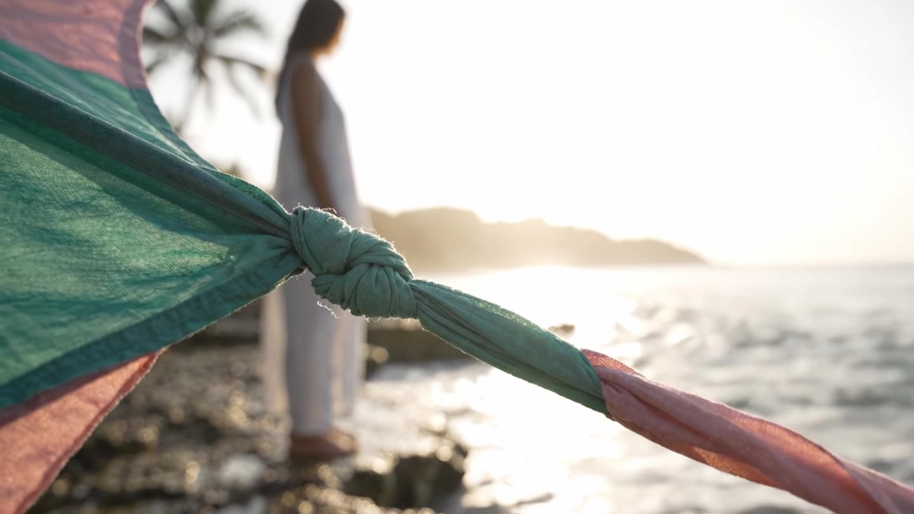 Un momento di riflessione: Una donna sta in piedi sulla riva mentre il sole tramonta, incorniciata da un colorato ombrellone da spiaggia e dalle dolci onde dell'oceano sullo sfondo.