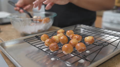 woman covers fresh donut holes in icing glaze and puts on cooling rack, slowmo