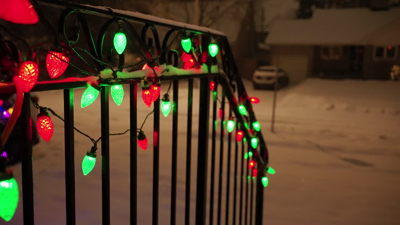 Red and green light bulbs on snowy railing, Christmas Eve, slow motion