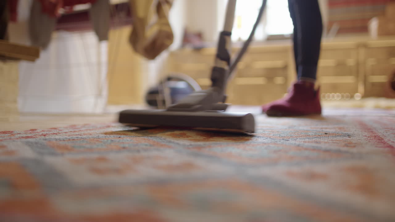 Housewife stay-at-home mom hoovering rug in living room, shallow focus low angle
