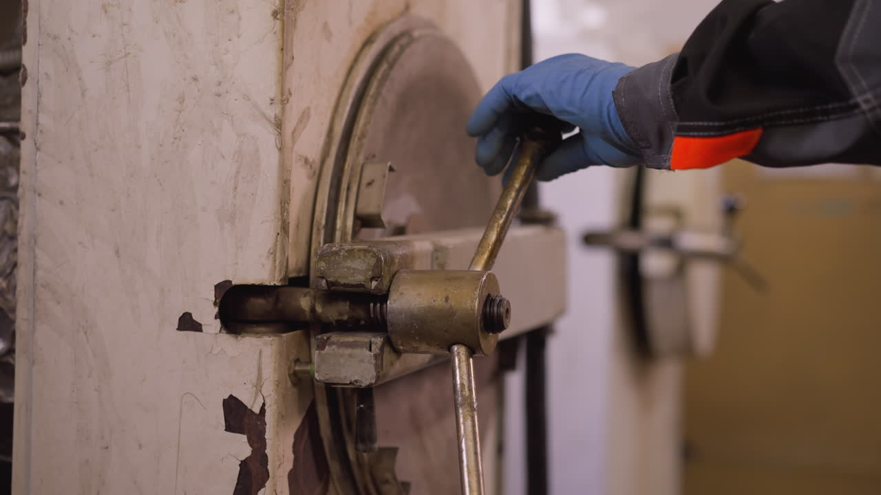 trabajador con mano con guantes que opera la palanca de la puerta del horno en un taller de cerámica, mostrando artesanía y trabajo manual