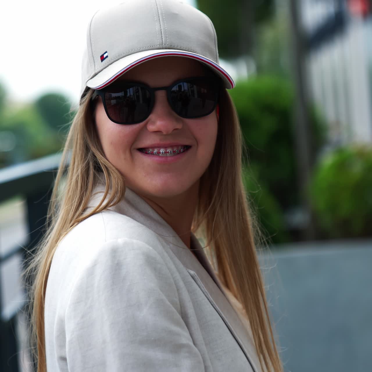 Smiling happy woman in black sunglasses and cap outdoors. Stylish fashionable young lady in the urban surrounding. Close up portrait