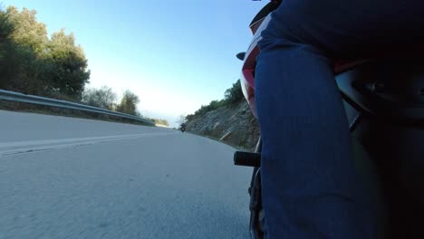 riding motorcycle in curvy mountain road, leaning through turns, view from left side behind riders leg