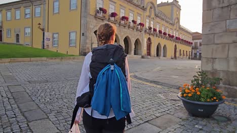 Beautiful-young-woman-rounds-corner-on-historic-cobblestone-road-as-sunrise-rays-pass-over-stone-buildings