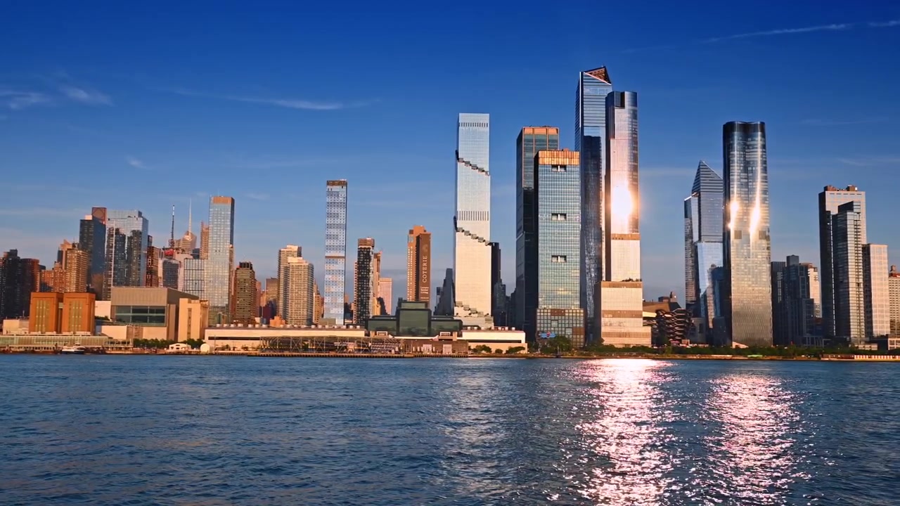Nova Iorque, EUA, 22 de maio de 2026: Horizonte de Hudson Yards visto do rio, Manhattan, Nova Iorque. Torres de vidro refletindo a luz do sol sobre água ondulada sob um céu azul claro.