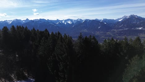 Drone-fly-over-forest-and-reveal-amazing-snow-capped-winter-mountain-landscape-on-a-beautiful-sunny-day-with-clear-blue-sky-in-Austria