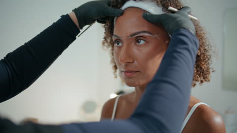 cosmetologist shaping woman brows in beauty salon closeup. curly girl visiting