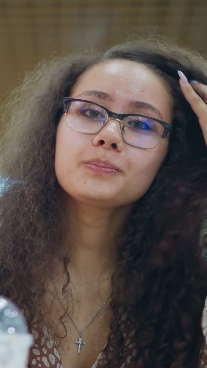 mujer beba una bebida cremosa con paja, ajustando su cabello y sonriendo en un centro comercial animado, creando un ambiente relajado y agradable con otra bebida cerca, fondo borroso y luces bokeh suaves