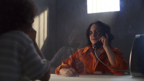 inmate and female visitor touching hands through glass during conversation