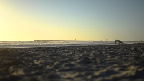 a close to the ground shot while a surfer walking along the beach towards the water with a surfboard in hand