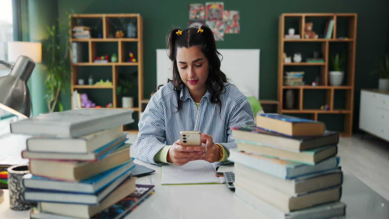 Woman using phone at desk with books