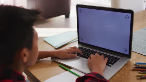 niño asiático en casa, sentado en la mesa para una lección escolar en línea usando una computadora portátil, con espacio de copia en la pantalla