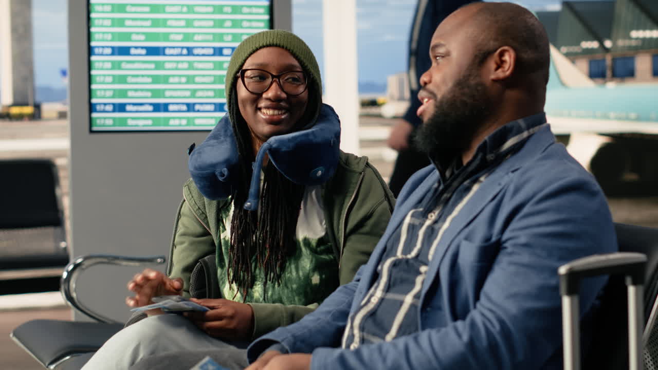 Coppia afroamericana in vacanza seduta insieme in un'area lounge dell'aeroporto.