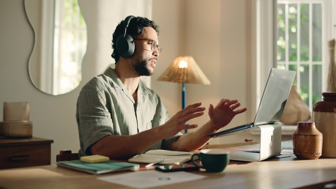 Man in Headphones Talking and Gesturing During Video Call on Laptop