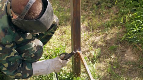 man in mask connects bottom details of fence by welding