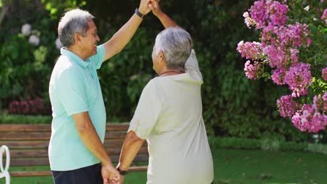 video of happy biracial senior couple holding hands and dancing in garden