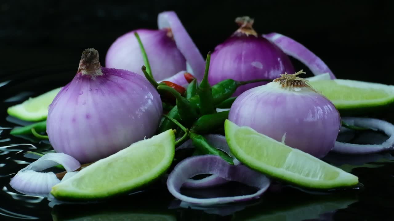 Static shot of slice of onions falling on lime and green chilli pepper
