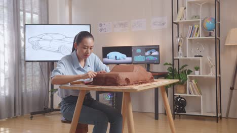 la diseñadora automotriz asiática trabaja en la escultura de arcilla de automóviles usando un cuchillo para suavizar la superficie y crear detalles en el diseño en el estudio