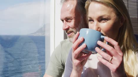 Happy-caucasian-mature-couple-drinking-coffee-and-talking-in-sunny-living-room