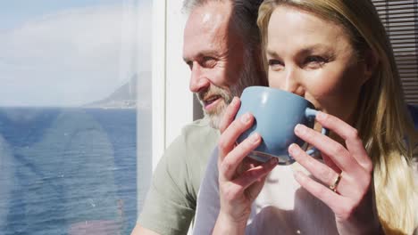 feliz caucásica pareja madura bebiendo café y hablando en la sala de estar soleada