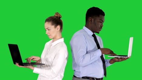 couple back to back standing and working on laptops on a green screen, chroma key