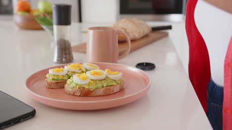preparing avocado toast with boiled eggs, asian woman adding seasoning in kitchen, at home