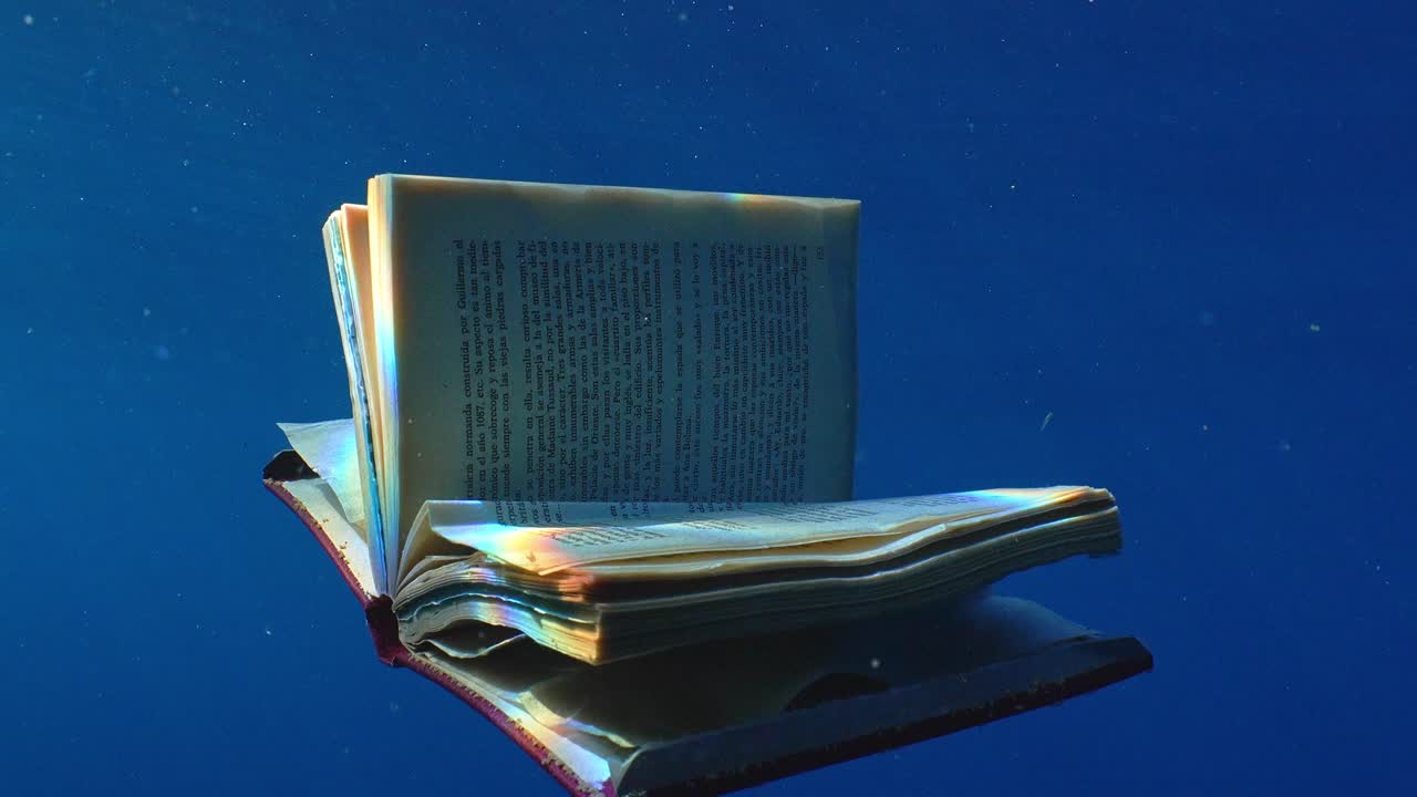 Abandoned book with open pages floating in blue water towards a boat in the ocean