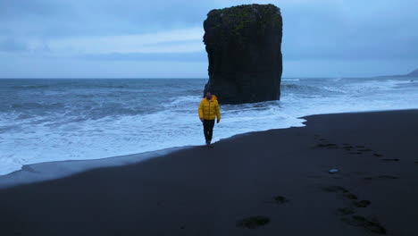 retrato frontal de un viajero masculino con chaqueta amarilla paseando por la playa de arena negra de laekjavik en islandia