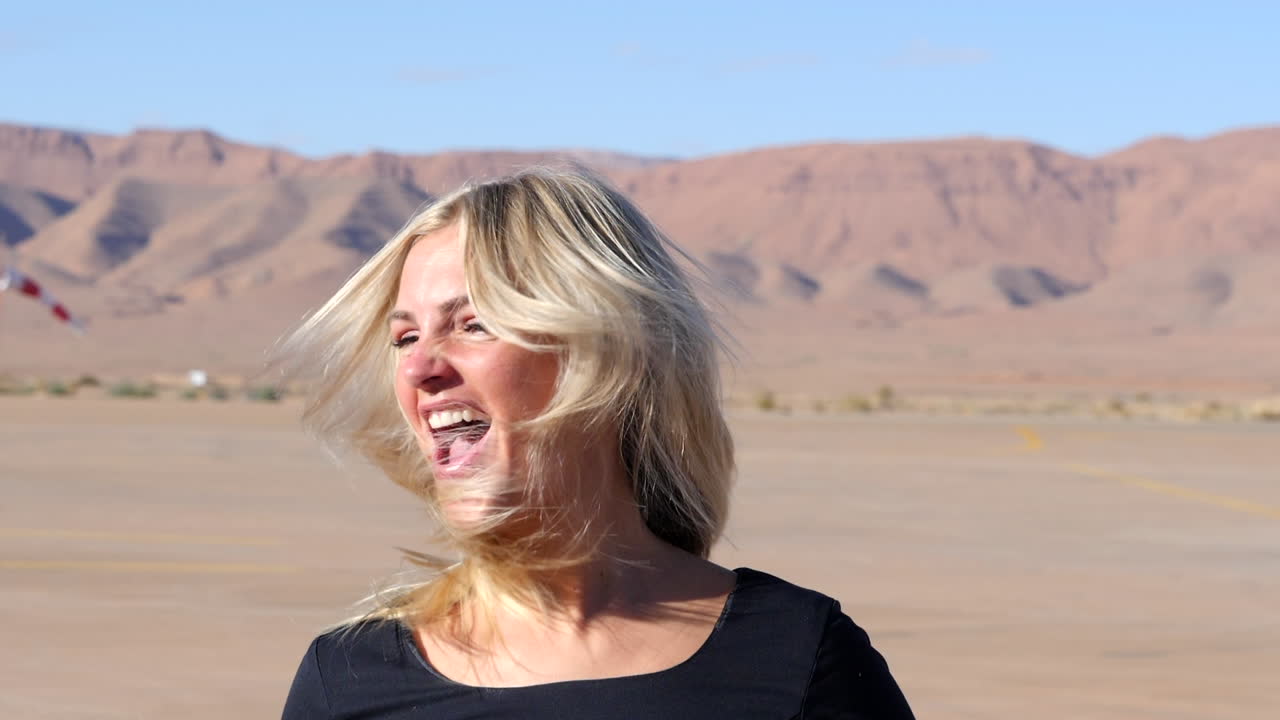 Primo piano di una gioiosa ragazza bionda che urla e agita i capelli, con montagne sfocate sullo sfondo, al rallentatore.