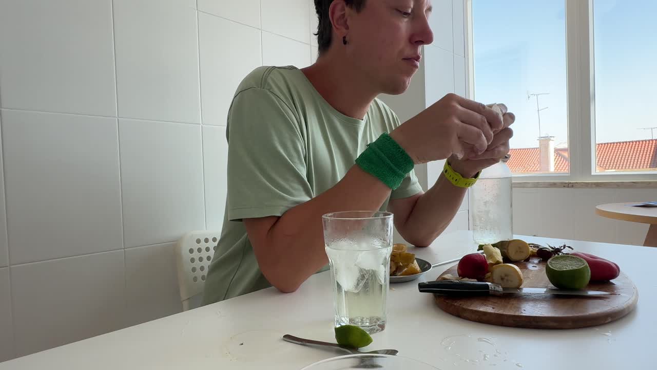 Junger Mann schält und isst Banane in einer hellen Küche.