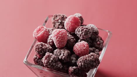 micro video of close up of raspberries in glass bowl with copy space on red background