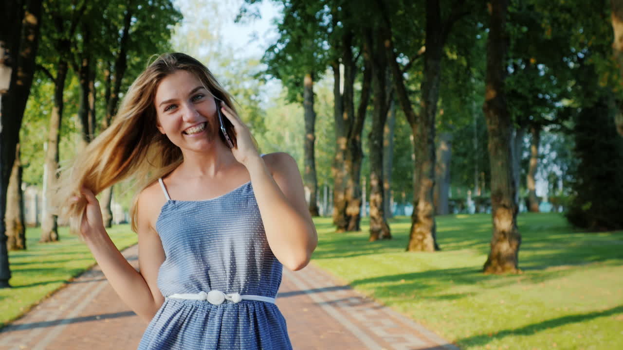 한 젊은 매력적인 여성이 여름날 9일 잘 정돈된 공원을 산책합니다.