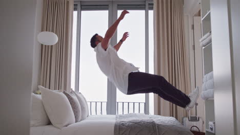 happy man jumping on bed resting after successful travel journey smiling enjoying independent lifestyle freedom