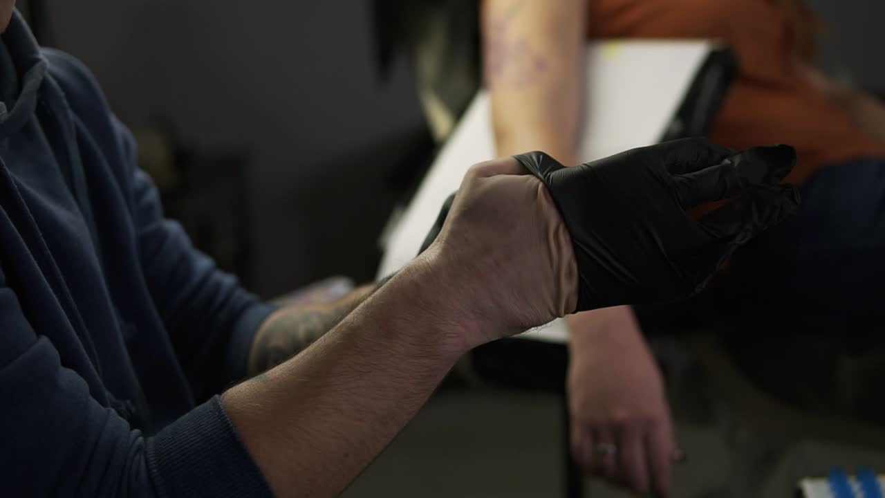 문신 가게에서 문신 세션 전에 라텍스 검은 장갑을 입는 손의 문신 예술가. 인식 할 수없는 고객 앞에 의자에 앉아있는 문신 예술가. 느린 움직임