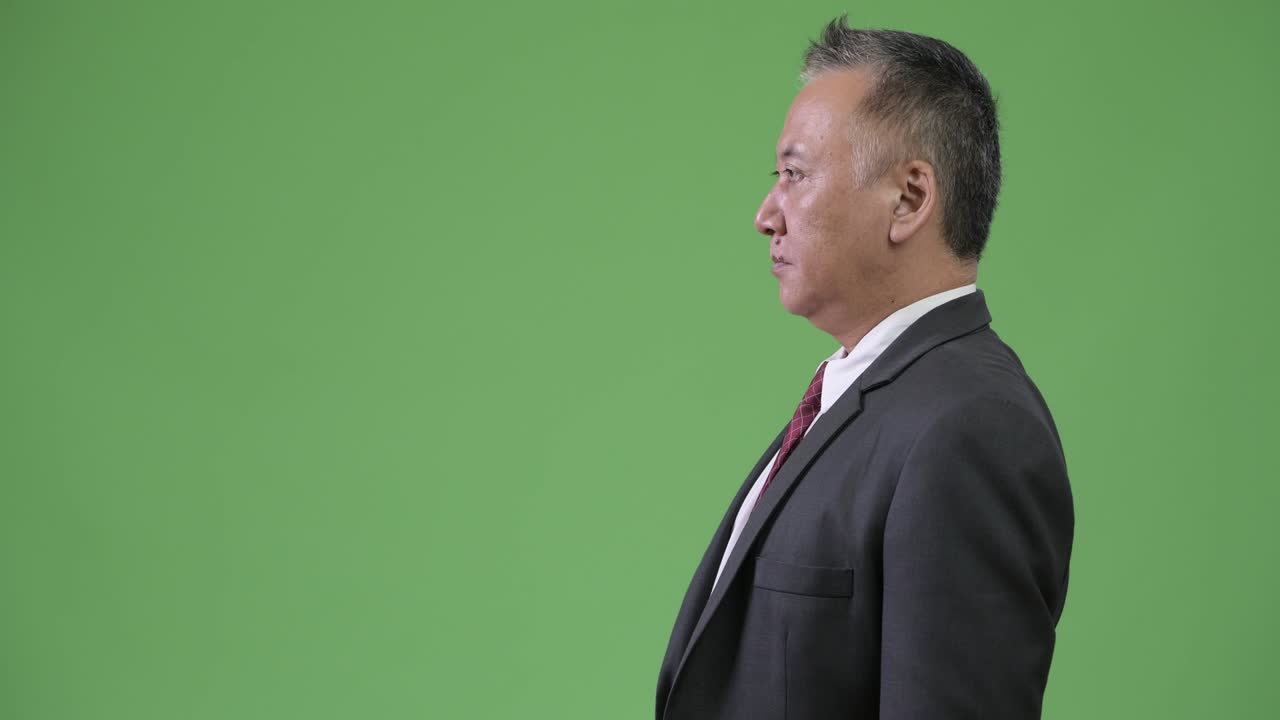 Profile view of mature Japanese businessman against green background