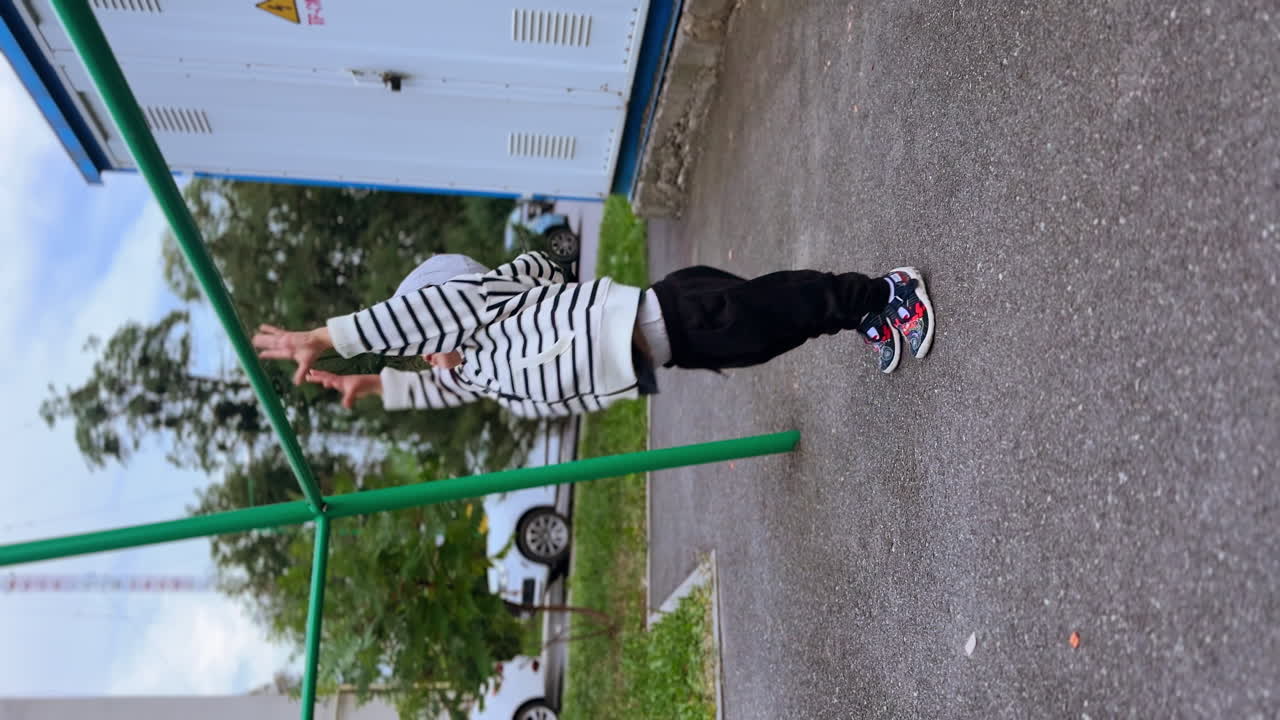 Little Caucasian toddler comes up to the horizontal bar. Healthy kid doing pull ups outdoors. Vertical view.