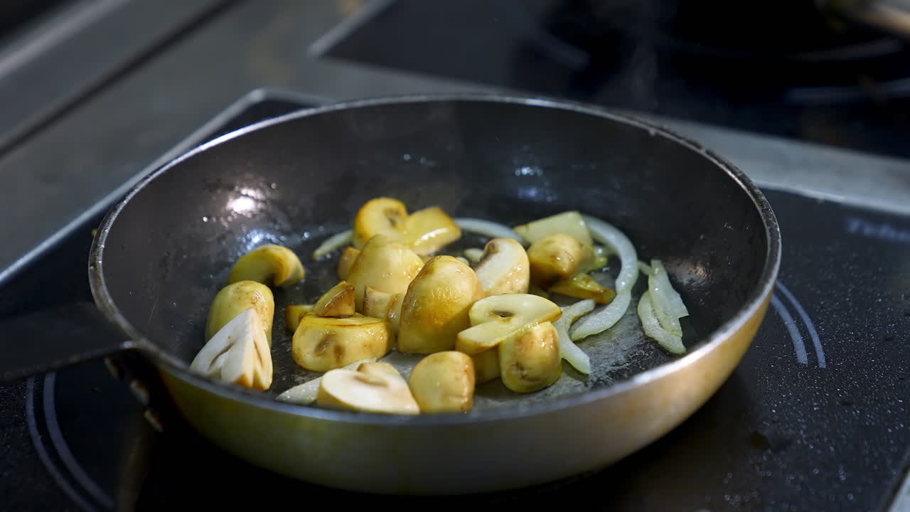 Cooking mushrooms in frying pan. Delicious mushrooms are frying with onions in oil on a stove. Close-up.