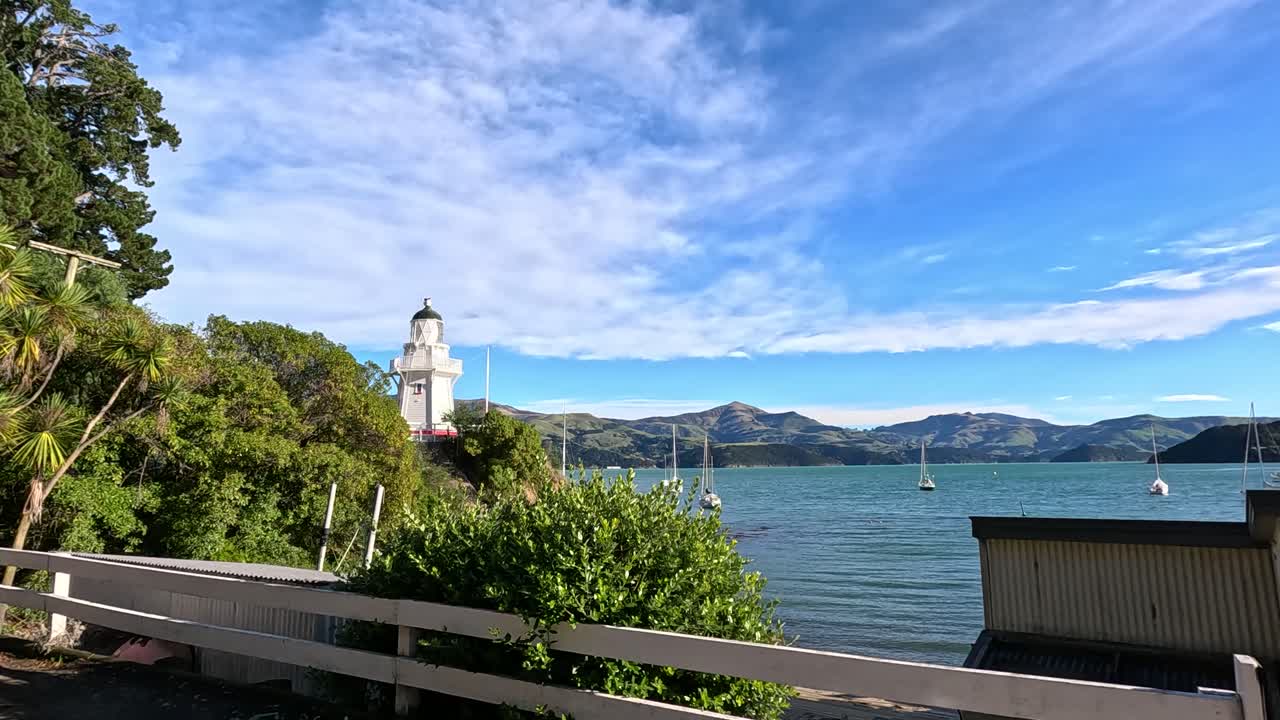 Aerial view of Akaroa's coastline with a lighthouse, captured during a sunny day drive