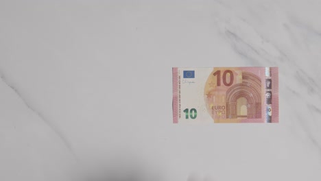 coup de monnaie aérien de main saisissant un billet de 10 euros sur une surface en marbre 1