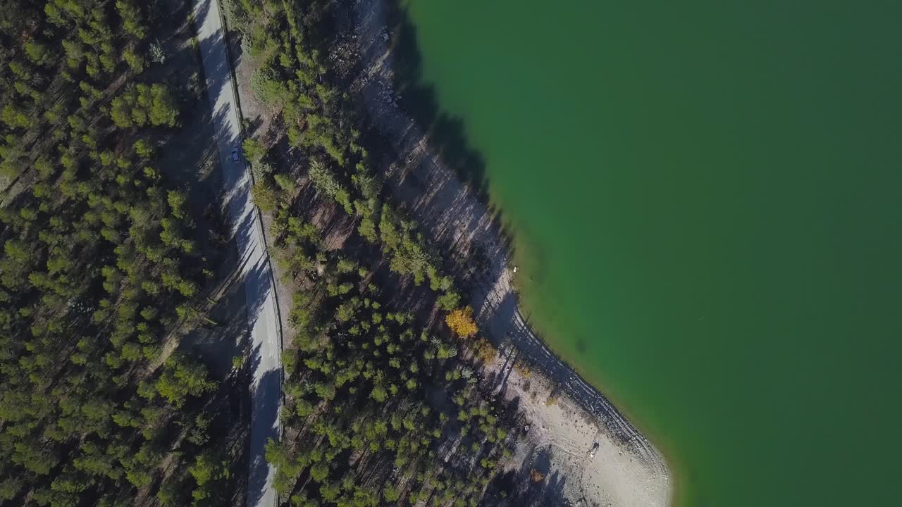 cámara siguiendo un coche conduciendo por una carretera en el bosque cerca de un lago