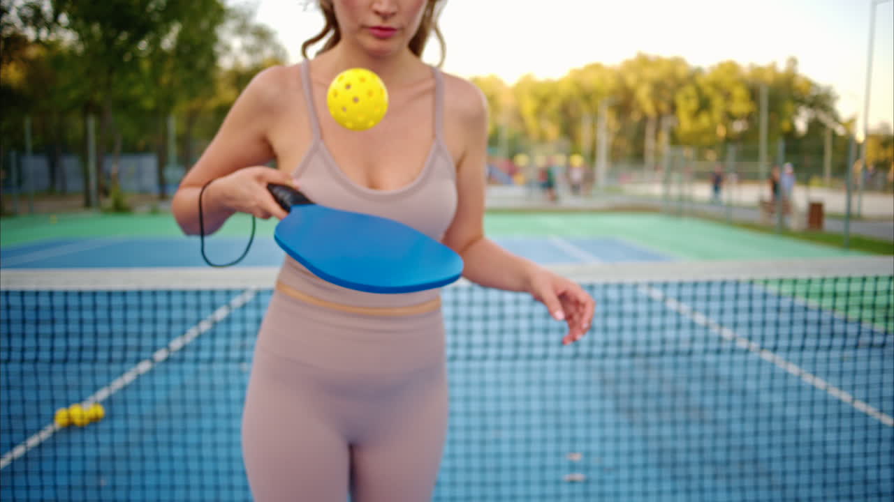 Woman playing pickleball with yellow ball and blue paddle at a court