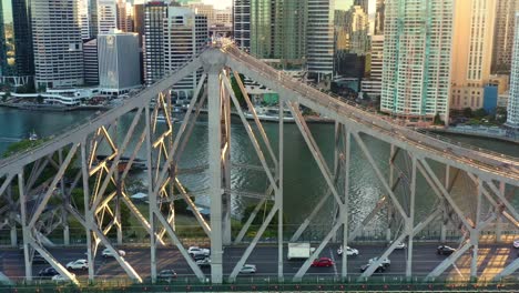 Filmische-Luftaufnahme-Bei-Sonnenuntergang,-Drohnenüberflug-Und-Rund-Um-Das-Historische-Wahrzeichen-Der-Stadt-Brisbane-Mit-Winzigen-Menschen-Auf-Einem-Abenteuerkletterweg-Auf-Die-Story-Bridge-Und-Verkehr,-Der-Den-Fluss-überquert