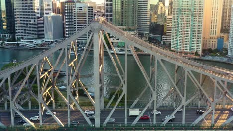 Toma-Aérea-Cinematográfica-Al-Atardecer,-Sobrevuelo-De-Drones-Y-Alrededor-Del-Monumento-Histórico-De-La-Ciudad-De-Brisbane-Con-Gente-Pequeña-En-Una-Aventura-Trepando-A-La-Cima-Del-Puente-De-La-Historia-Y-Los-Tráficos-Que-Cruzan-El-Río.