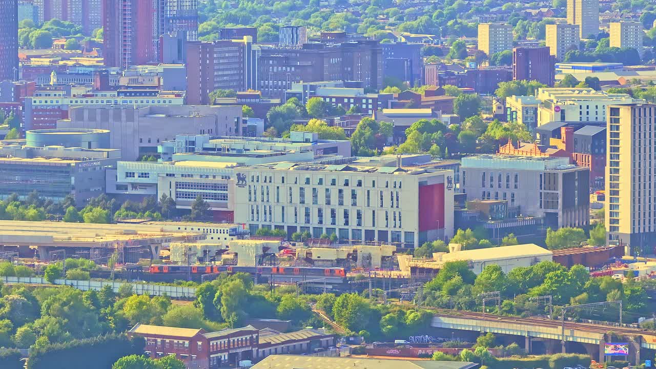 Aerial Perspective of Birmingham City Centre Showing Modern Architecture, a cargo train passing and Green Spaces Under Warm Sunlight