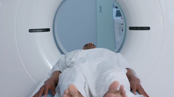 Console is initiating table, moving adult male remaining still into CT gantry in clinic for CT