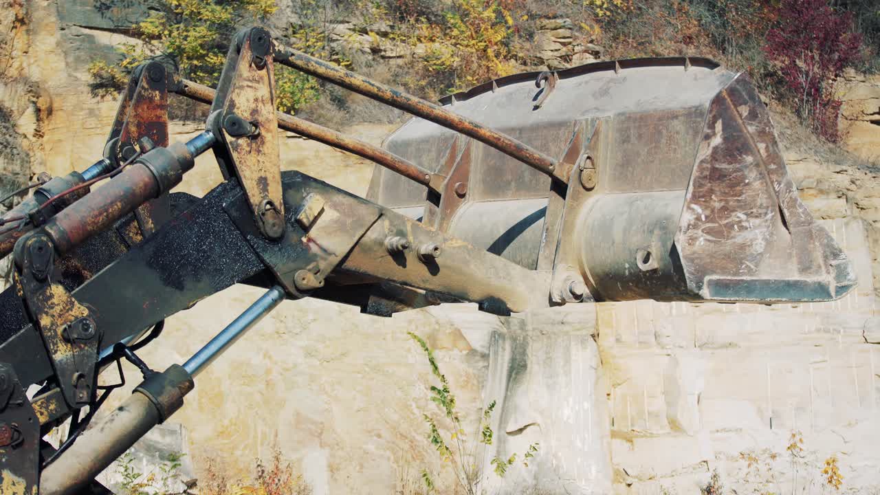 An old rusty yellow excavator with a large bucket is working on a stone quarry