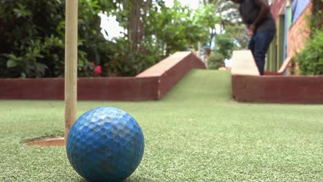 Tiro-Cercano-Y-Bajo-De-Una-Pelota-De-Golf-Que-Se-Astilla-Sobre-Un-Obstáculo-Y-Golpea-El-Pin-En-El-Green-En-El-Campo-De-Minigolf