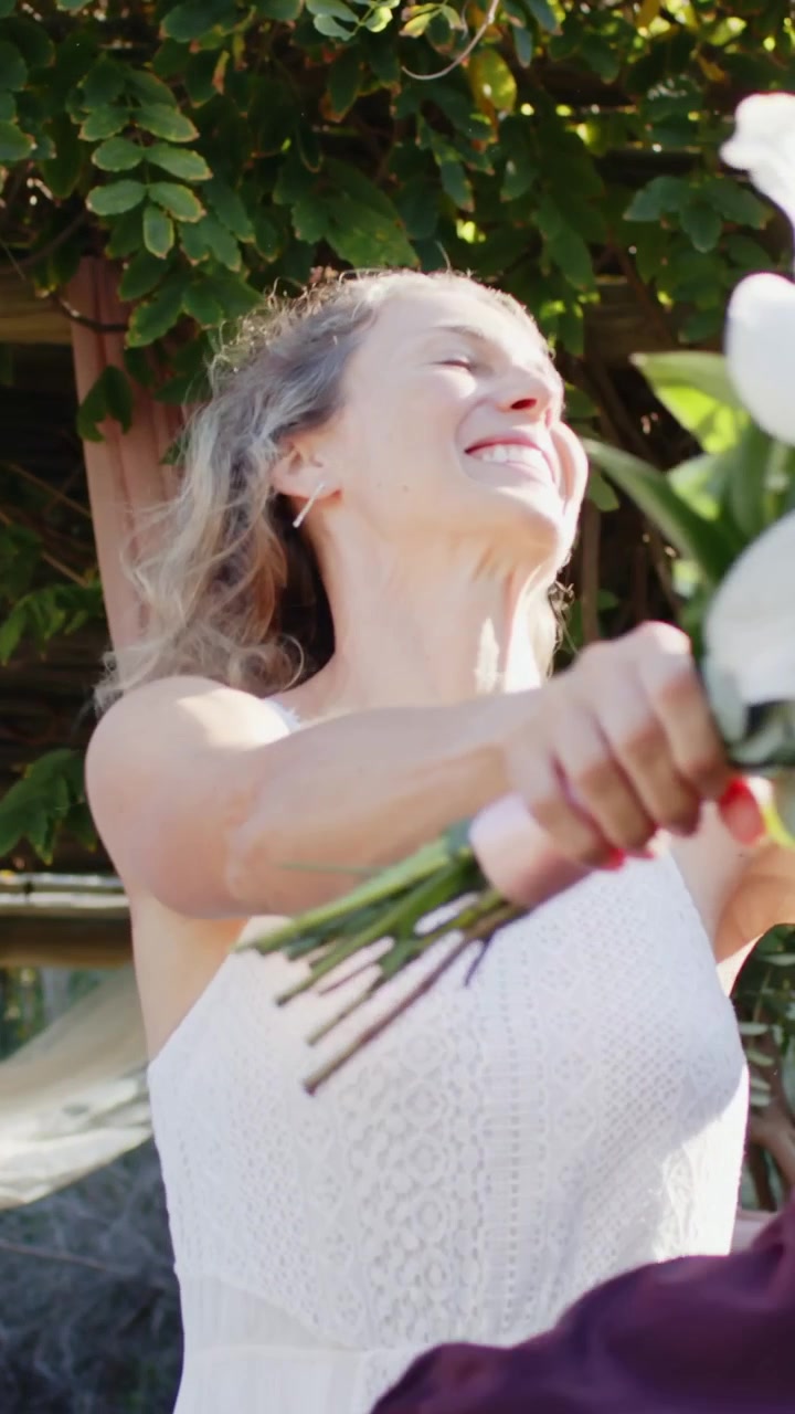 Video verticale: Donna in abito bianco che regola la presa, presso un traliccio da giardino, offre gigli al partner.