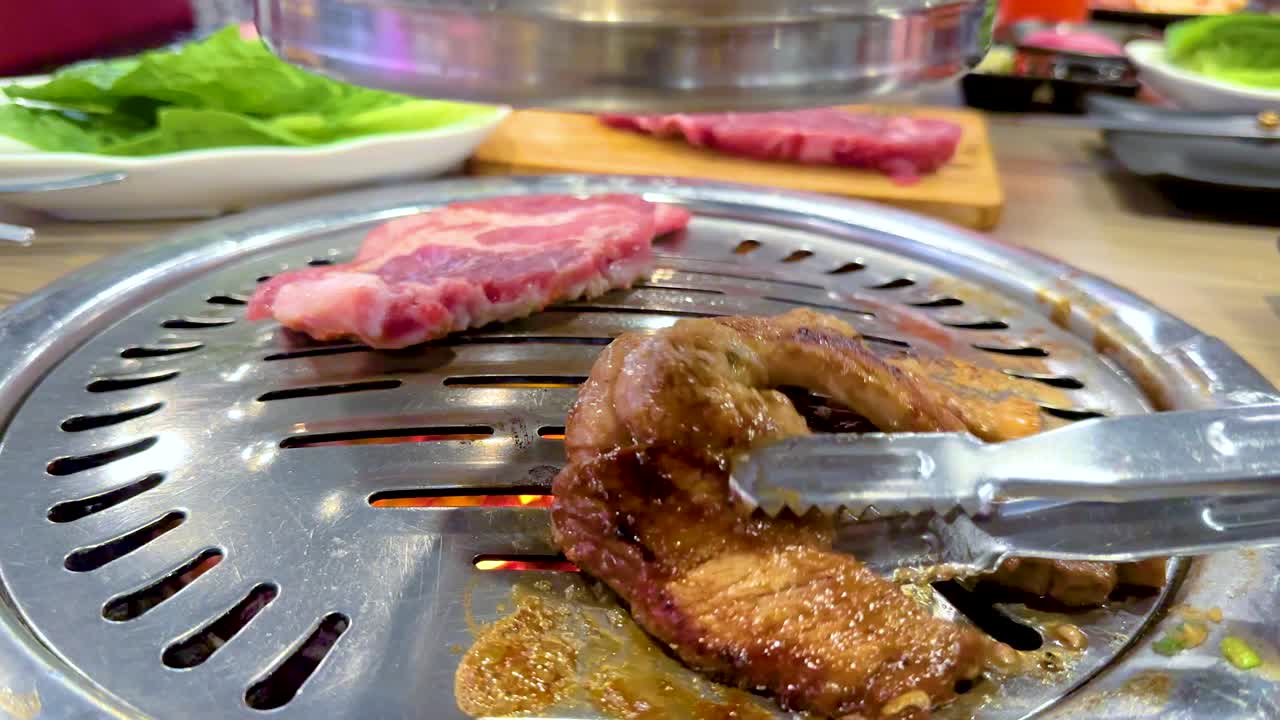 Close-up of meat grilling on a Korean BBQ in Bangkok. Vibrant colors and dynamic action captured in a lively dining setting